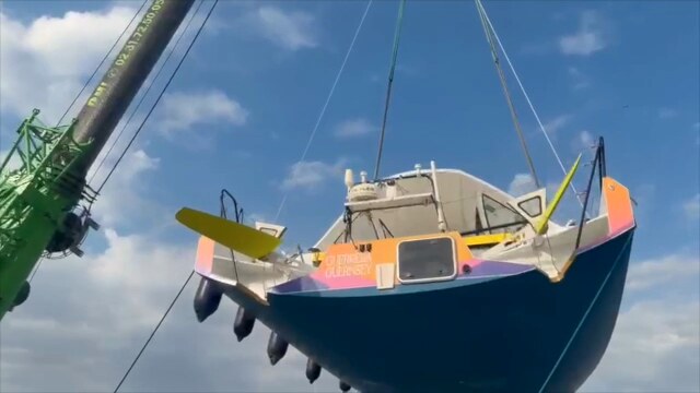 Guerrera suspended by travel lift against a blue sky, canting keel and rudders visible